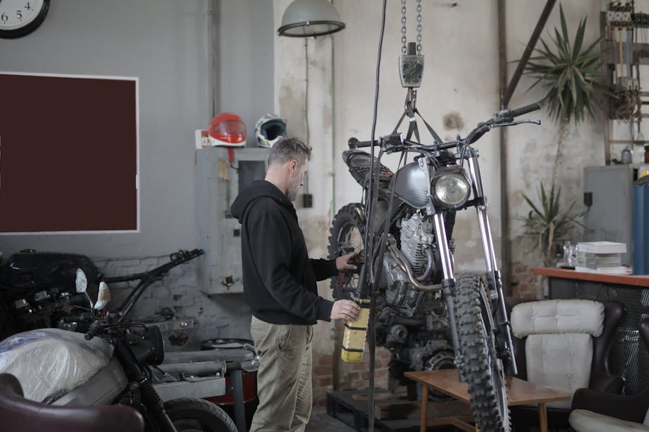 Mechanic working on a motorcycle in an industrial workshop, performing maintenance tasks.